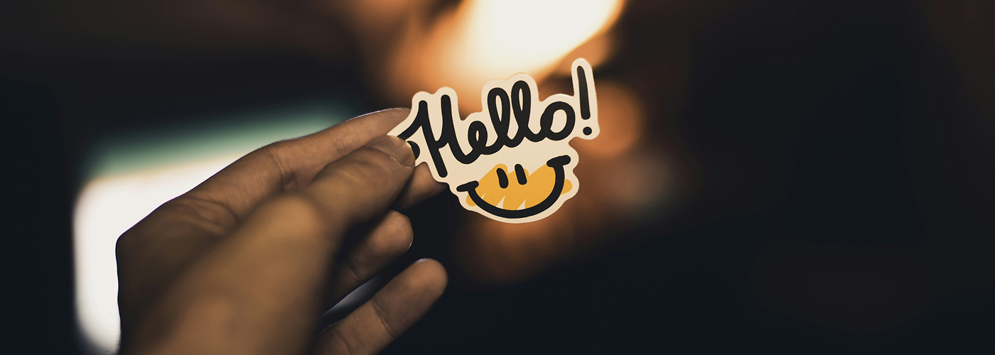 Hand holding 'Hello!' sticker with smiley face