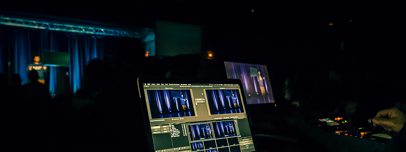Dark stage with audience and large screens at virtual-hybrid event